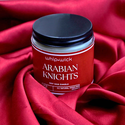 Whipandwick Arabian Knights soy wax candle in a red glass jar, lit and surrounded by deep red roses against a dark, elegant background.