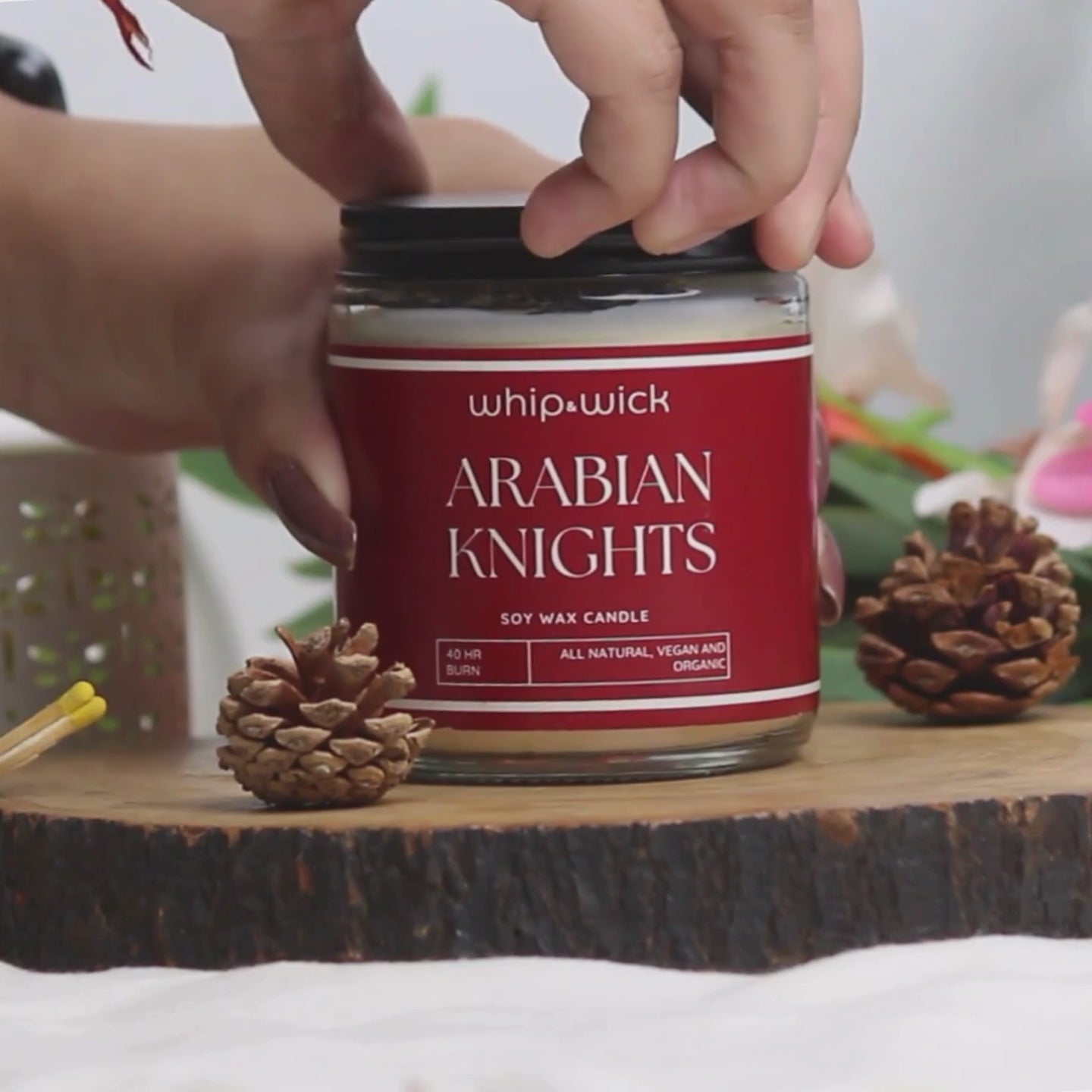 Whipandwick Arabian Knights soy wax candle in a red glass jar, lit and surrounded by deep red roses against a dark, elegant background.